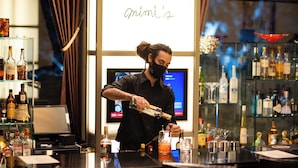 A bartender preparing a drink at a bar with a variety of liquor bottles and glasses. - Phoenix Hotel (Hakuba)