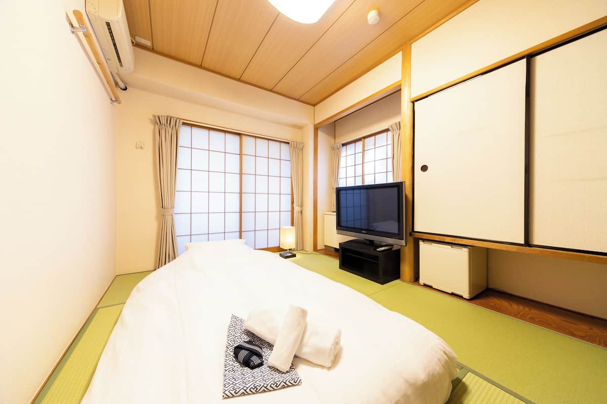Habitación de hotel con cama, televisión, refrigerador pequeño y armario con puerta corredera.