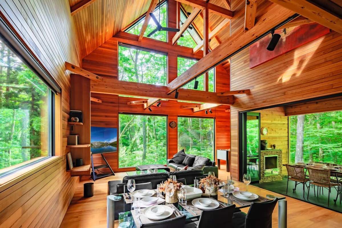 Una cabaña de madera moderna con ventanas amplias, comedor y chimenea.