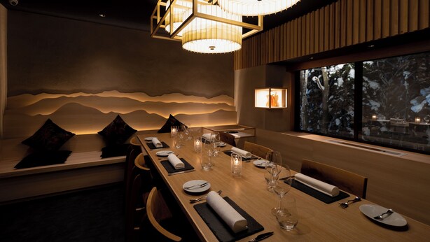 A dining area with a long wooden table set for a meal, a bench with cushions, and a view of trees through large windows. - Phoenix Hotel (Hakuba)