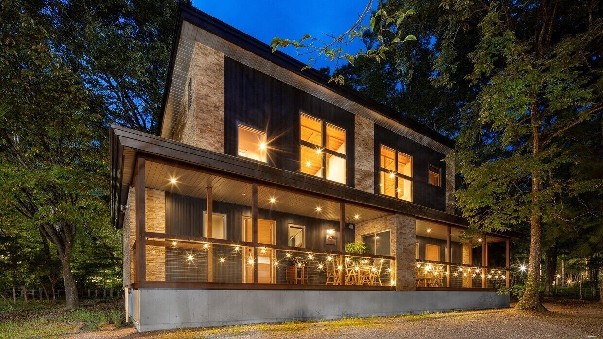 A modern two-story house with large windows, a balcony, and a stone facade.