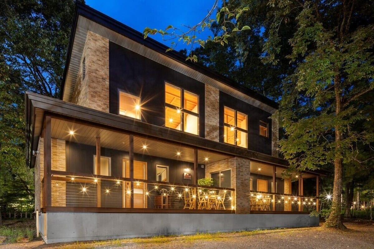 Una casa moderna de dos pisos con amplios ventanales, un balcón y fachada de piedra.