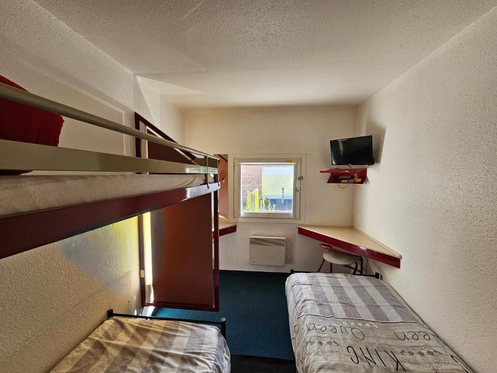 Une chambre de dortoir équipée de lits superposés, d’un bureau, d’une chaise, d’une télévision et d’une fenêtre donnant sur un paysage agréable.