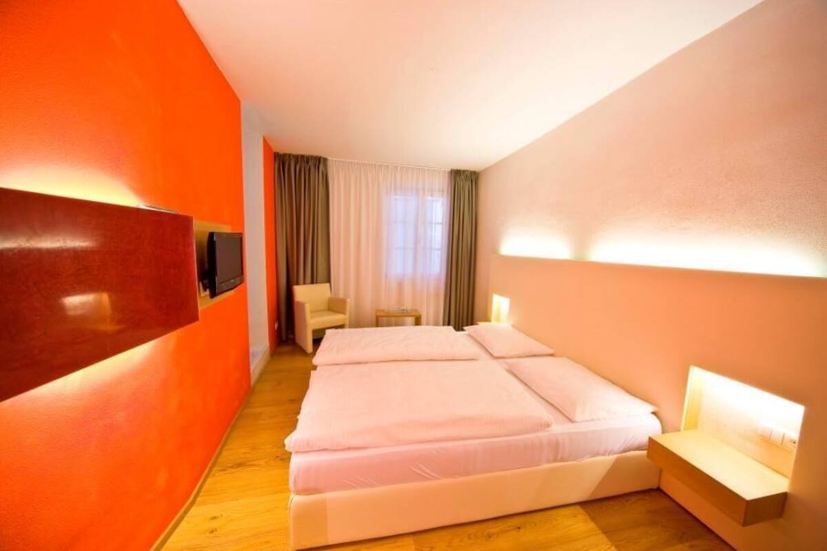 A hotel room with a large bed, a TV mounted on the wall, and a seating area with a chair and table.