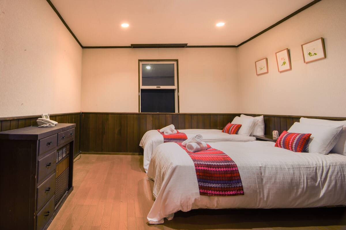 A hotel room with two beds, a desk, and a window.