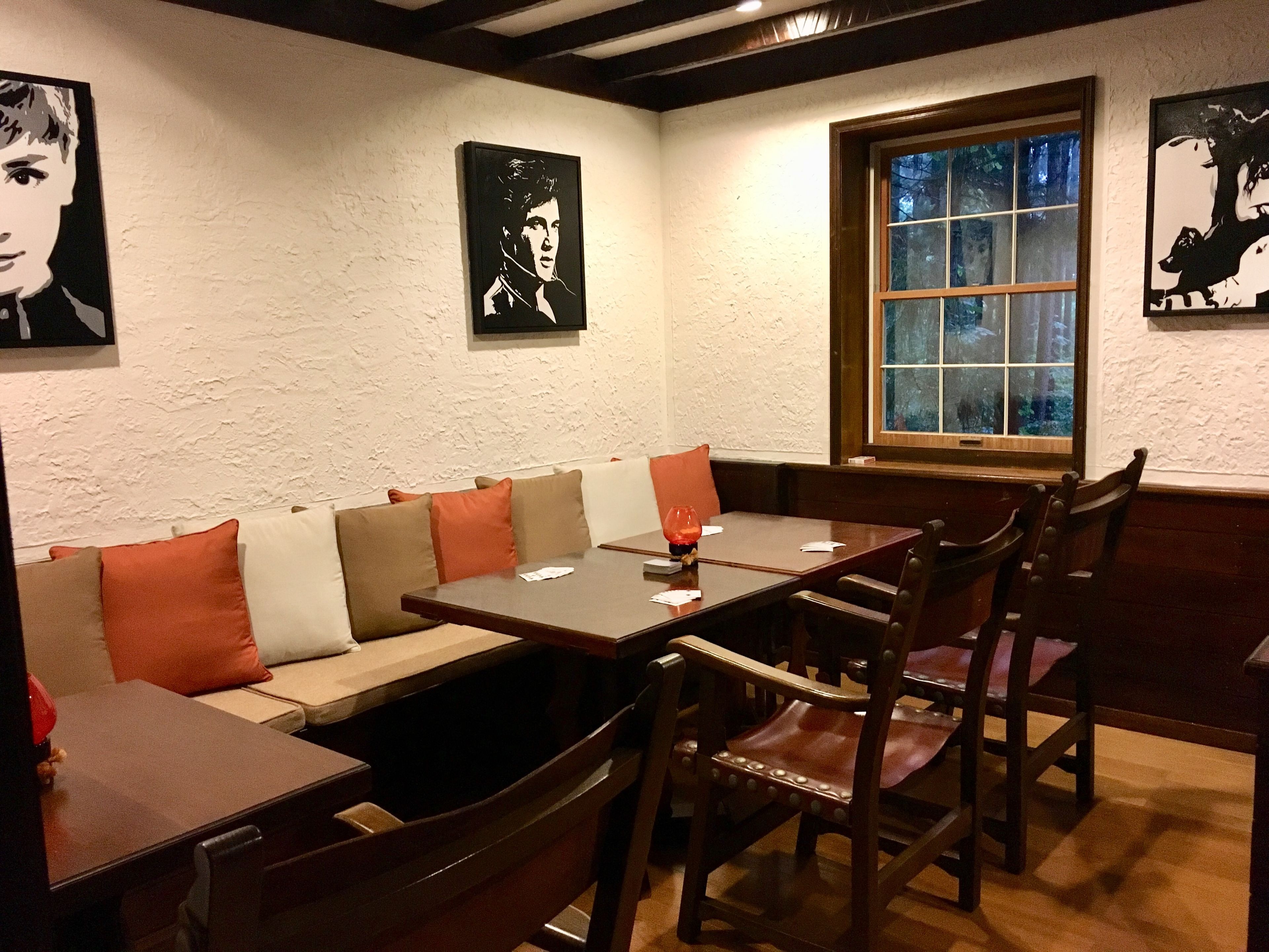 A restaurant interior with booths, wooden tables, and chairs. There are framed pictures on the walls.