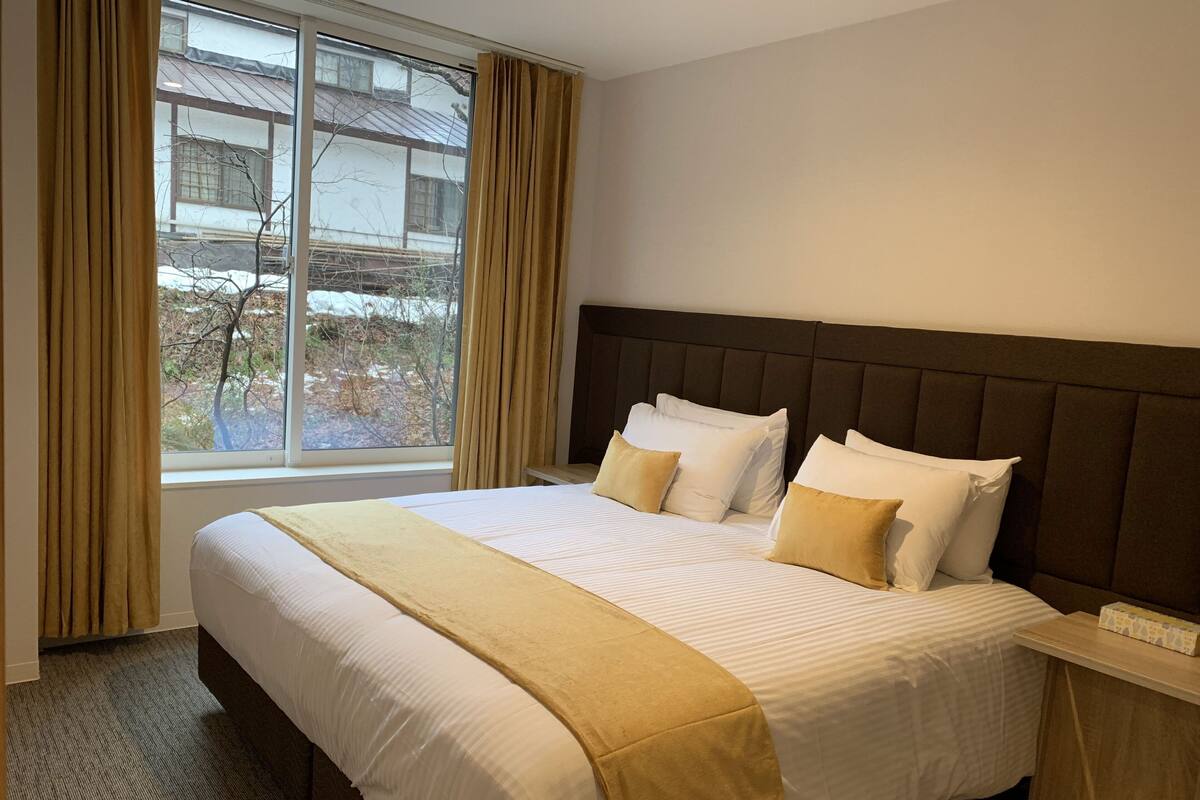 A hotel room with a large bed, a headboard, a bedside table, and a window with curtains.