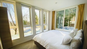 Ein Schlafzimmer mit einem großen Bett, mehreren Fenstern und Blick ins Freie.
