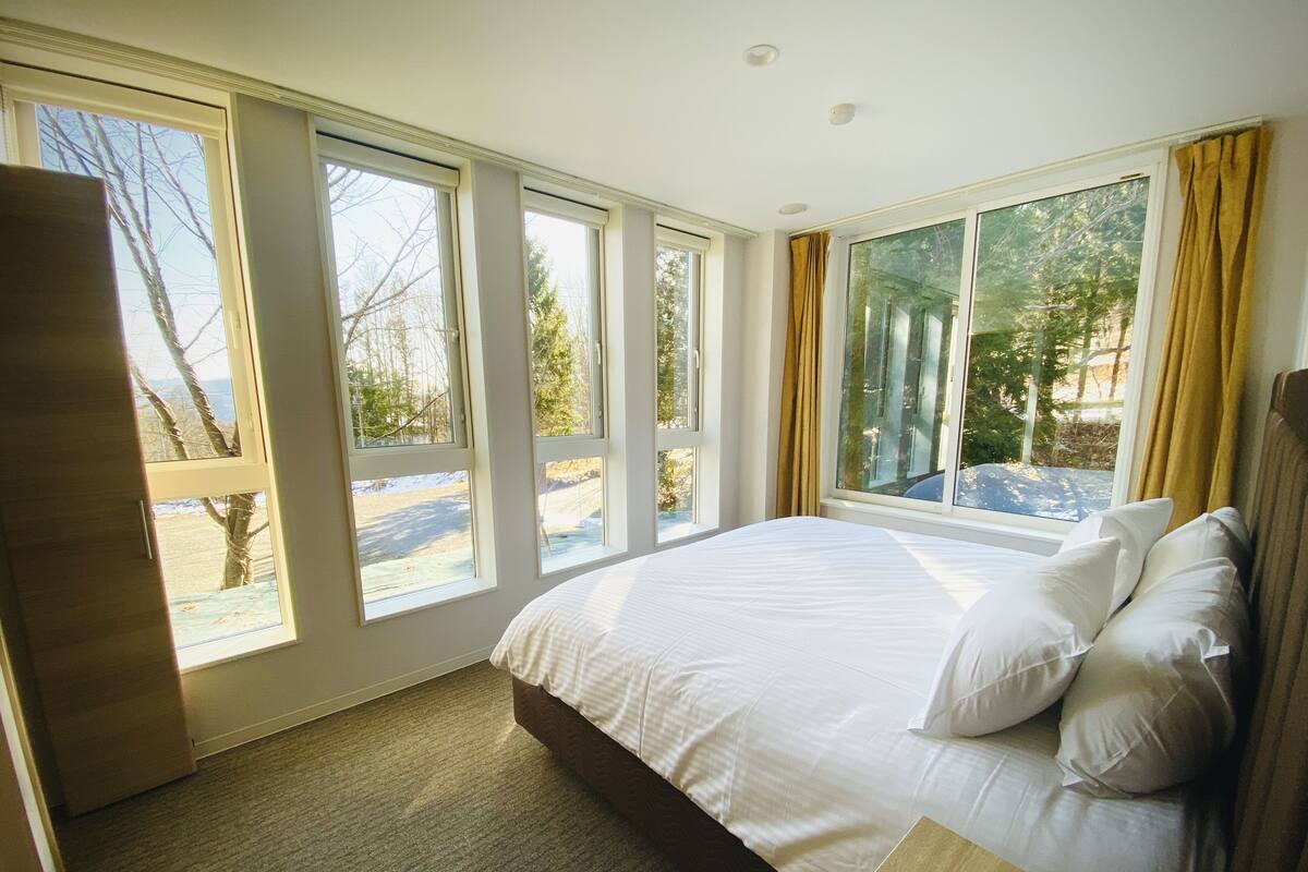 A bedroom with a large bed, multiple windows, and a view of the outdoors.