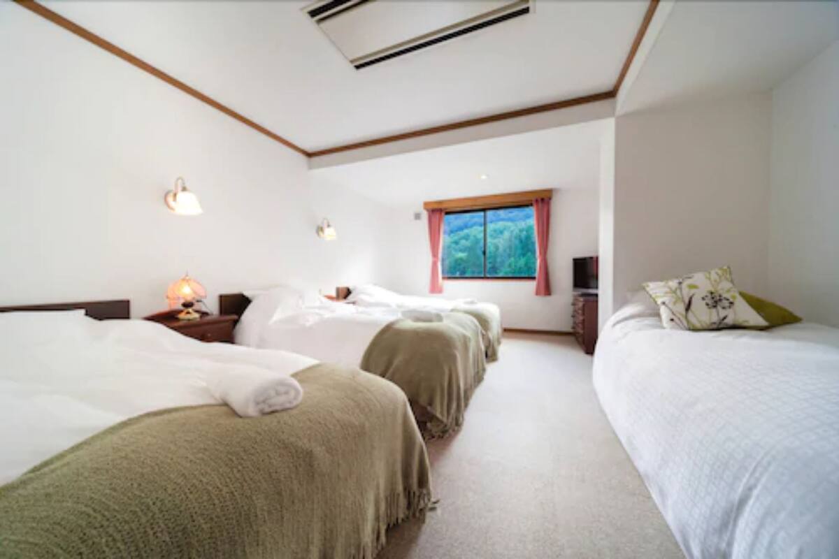 A hotel room with three beds, a window with pink curtains, and a ceiling fan.