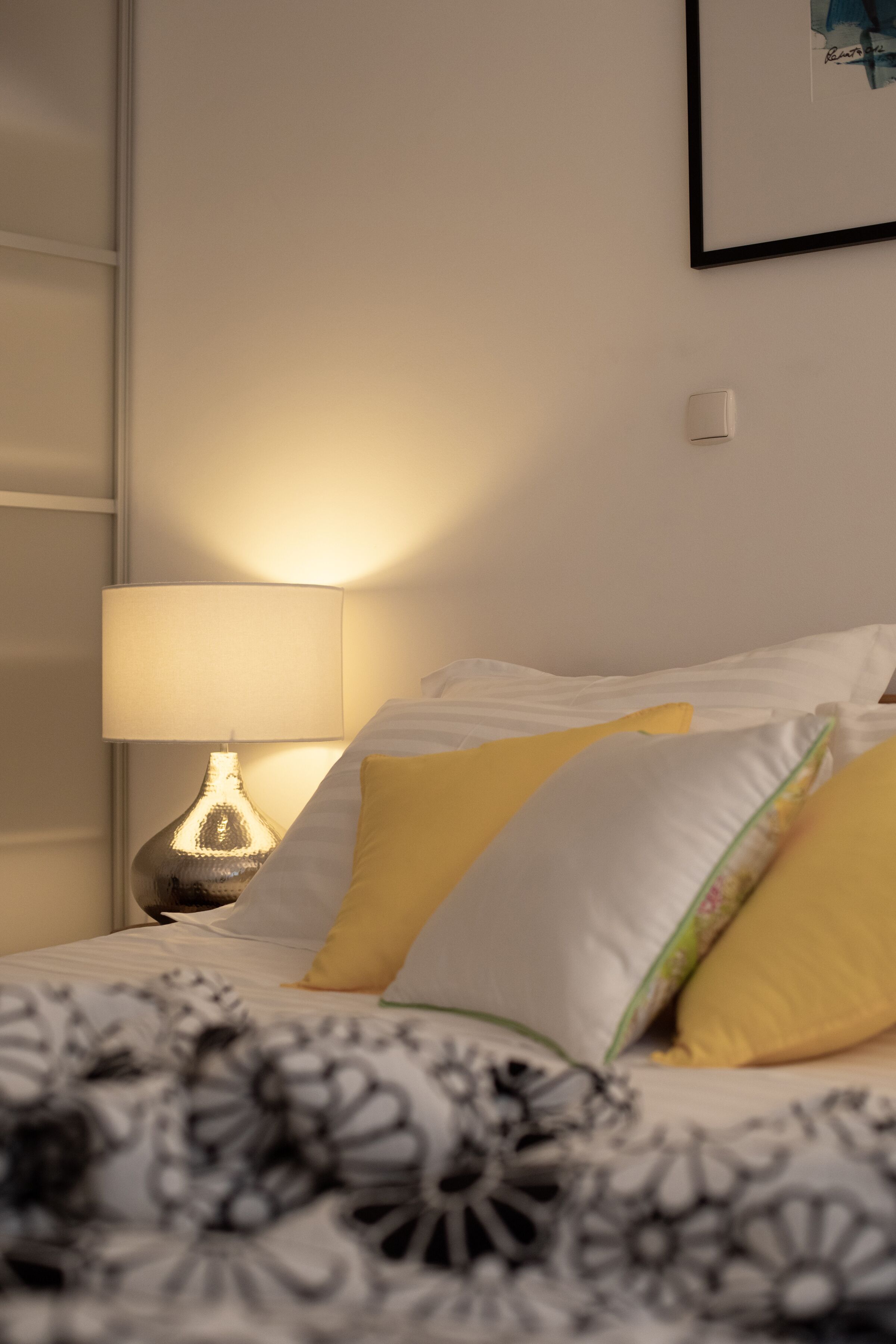 A neatly made bed with white and yellow pillows, a patterned blanket, and a bedside lamp.