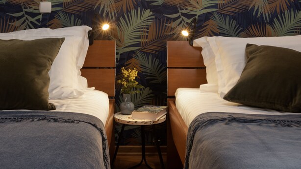 A hotel room with two beds, a small table with a vase, and a patterned wallpaper. - Luxe Dubrovnik Apartments (Dubrovnik)