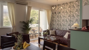 A living room with a brown leather sofa, a dining table with chairs, a potted plant, and a view of the outdoors through a sliding glass door. - Luxe Dubrovnik Apartments (Dubrovnik)