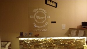 Una recepción con fachada de piedra, un letrero que dice "Tarsan Apartments desde 2007, bienvenidos" y un pequeño certificado enmarcado en la pared.