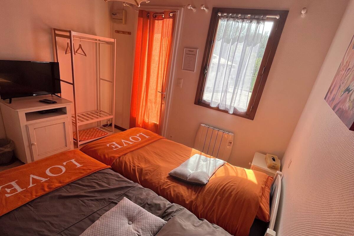 A bedroom with two beds, a TV, a wardrobe, and a window with curtains.
