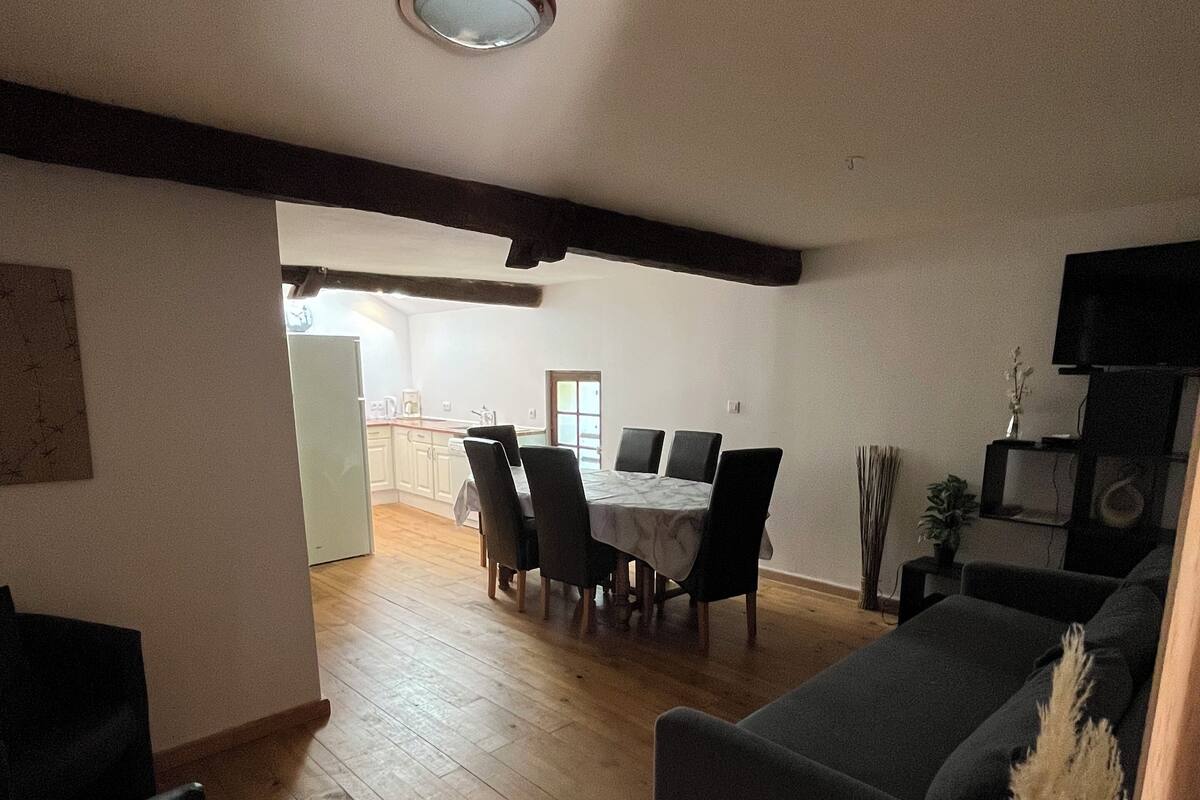 A living room with a dark sofa, a dining area with a table and chairs, wooden flooring, and a ceiling light fixture.