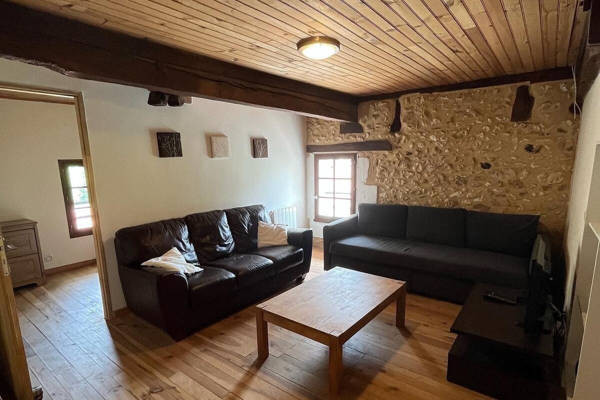 A cozy living room with wooden flooring, a stone wall, and two dark sofas.