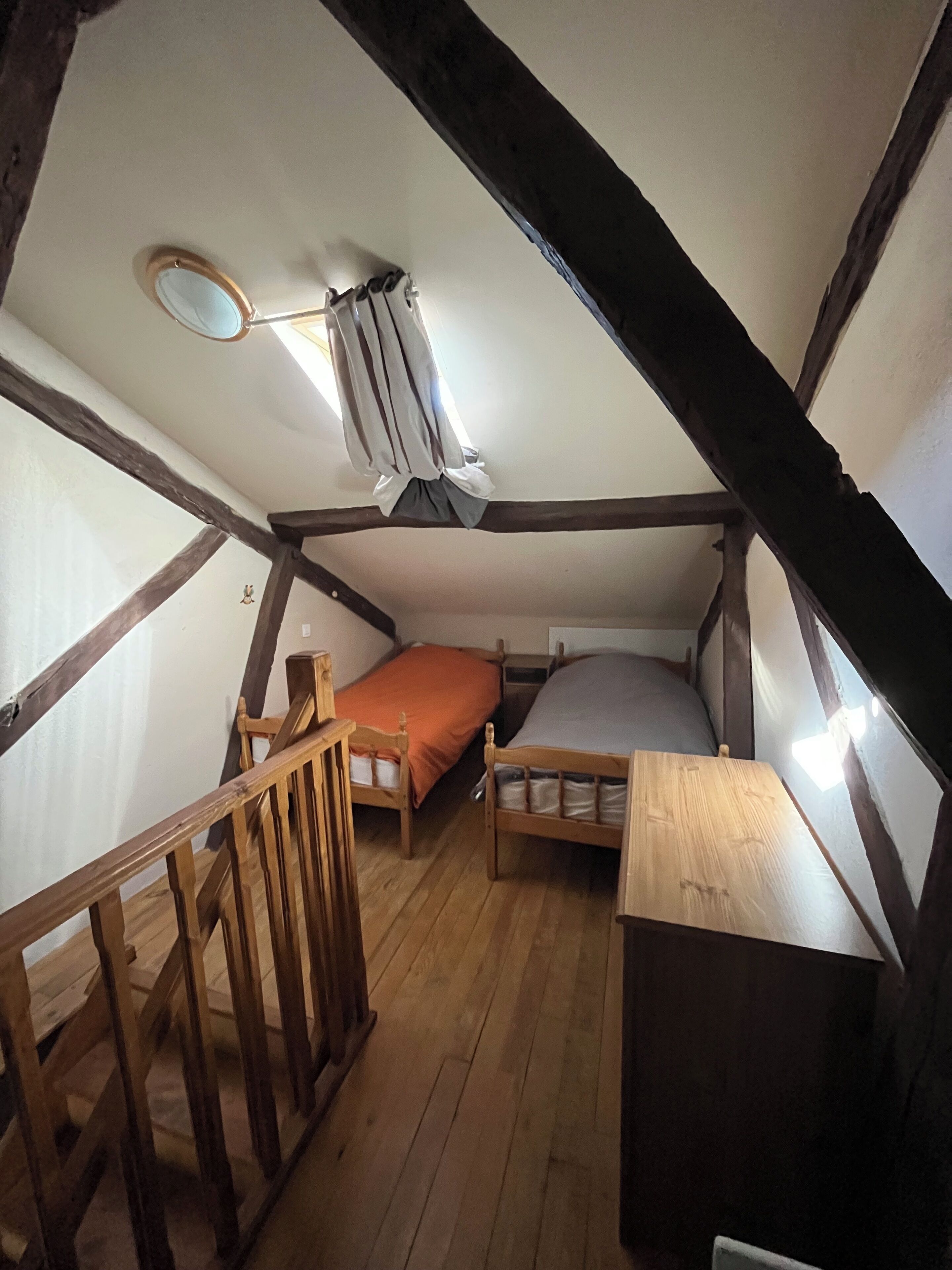 A small attic bedroom with two wooden beds, a wooden desk, and a slanted ceiling.