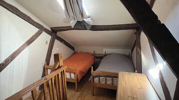A small attic bedroom with two wooden beds, a wooden desk, and a slanted ceiling.