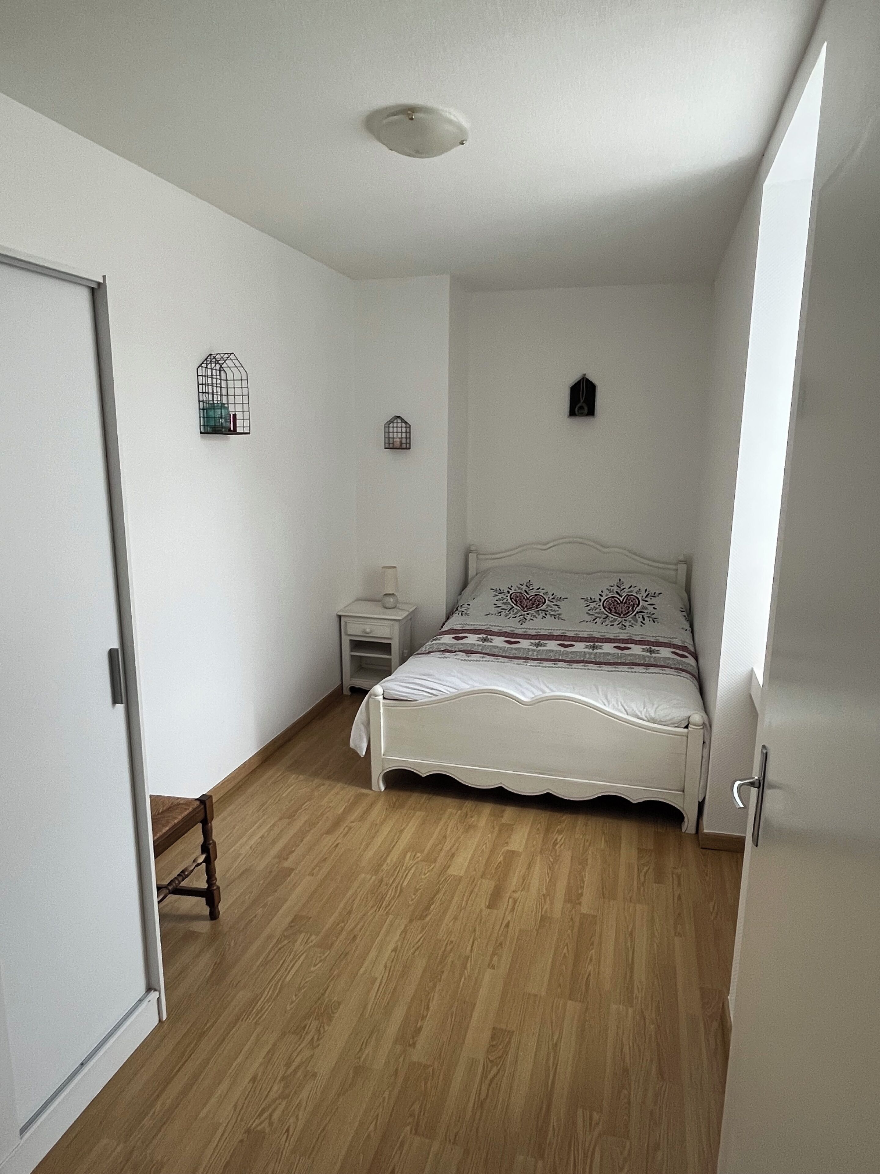 Een slaapkamer met een houten vloer, een bed met een decoratieve hoofdbord, een nachtkastje en twee aan de muur bevestigde vogelkooien.
