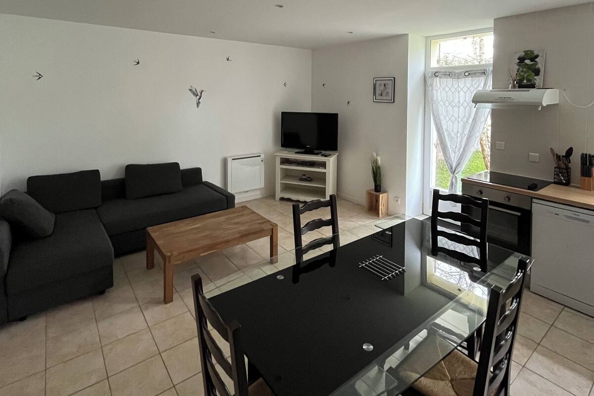 A modern living room with a black sofa, a glass dining table, and a TV on a white stand.