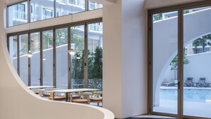 A modern hotel lobby with a curved reception desk, large windows offering views of the pool and outdoor seating, and a multi-level ceiling design. - Terra Nara (Pattaya)