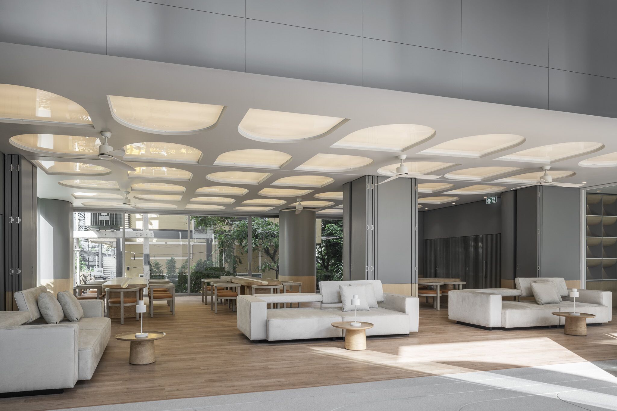 A modern lounge area with a high ceiling, recessed lighting, and a mix of seating arrangements including sofas and tables.