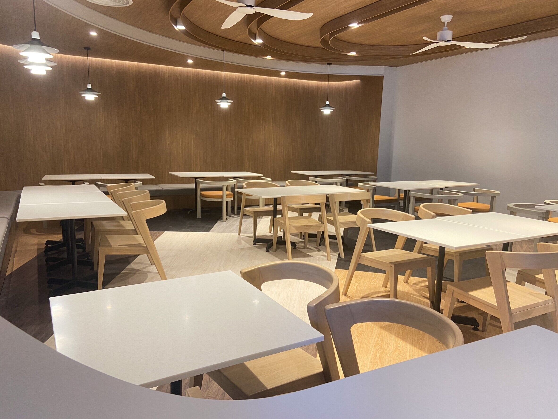 A modern dining area with wooden tables and chairs, recessed ceiling lighting, and a curved ceiling design.
