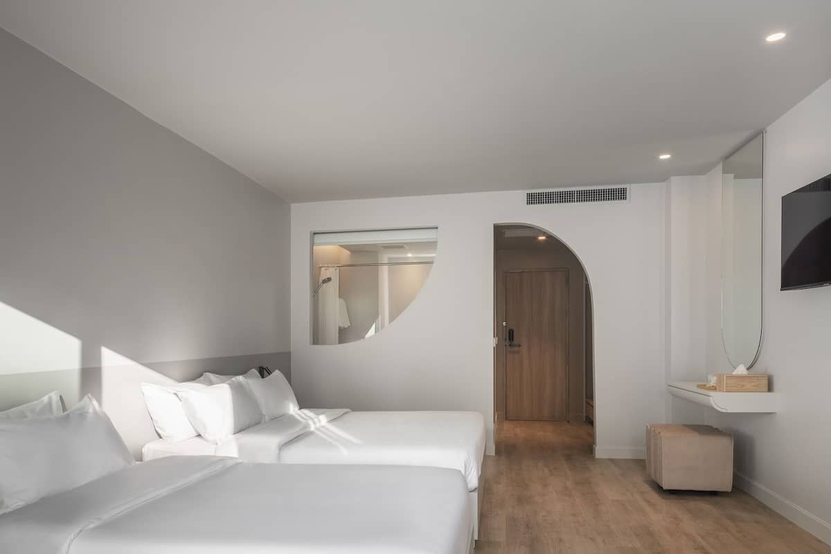 A modern hotel room with two beds, a large mirror, a TV, and a wooden door leading to a bathroom.