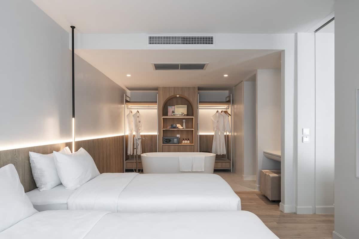 A modern hotel room with two beds, a walk-in closet, and a TV.