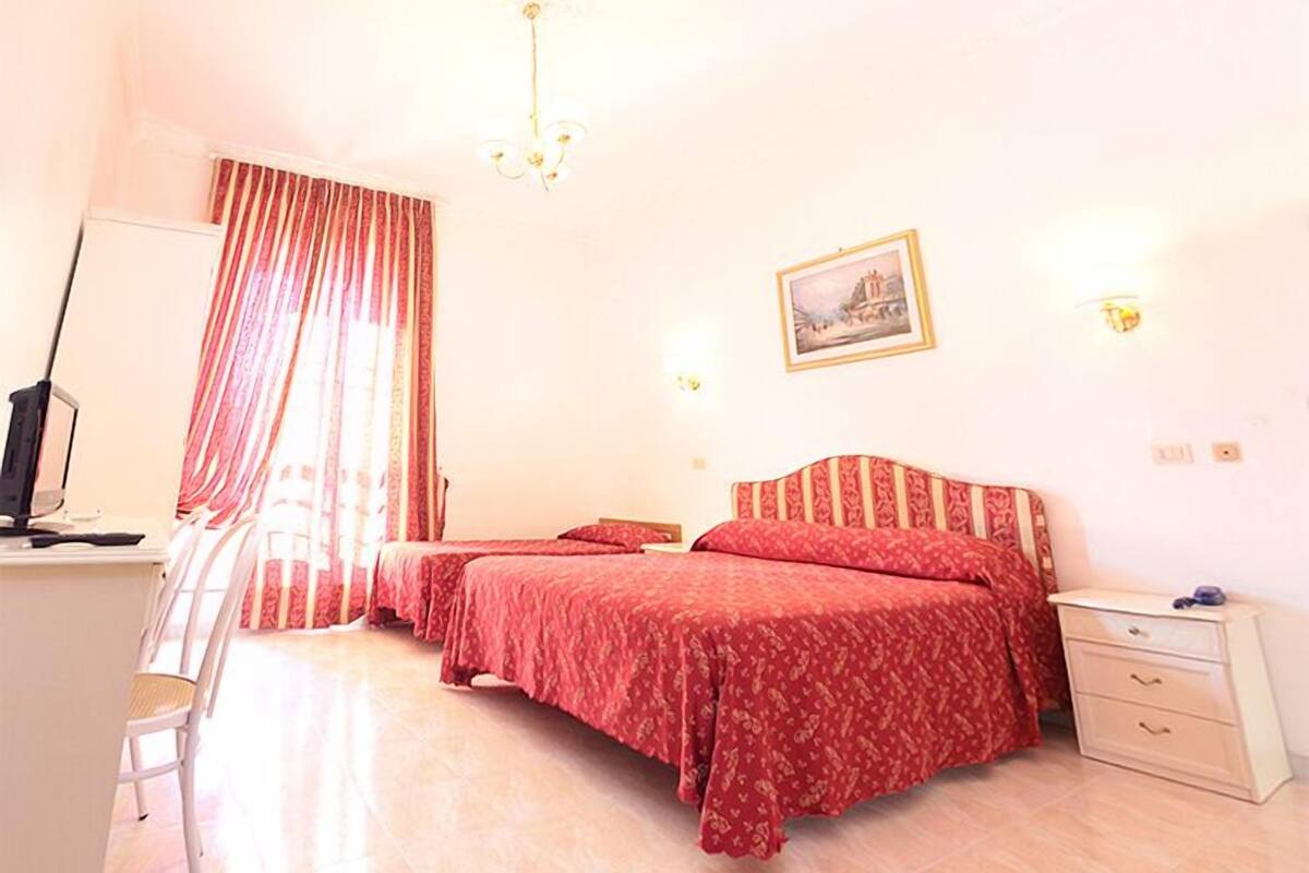 Une chambre avec deux lits, un bureau avec un ordinateur, une chaise, une table de chevet et un tableau au mur.