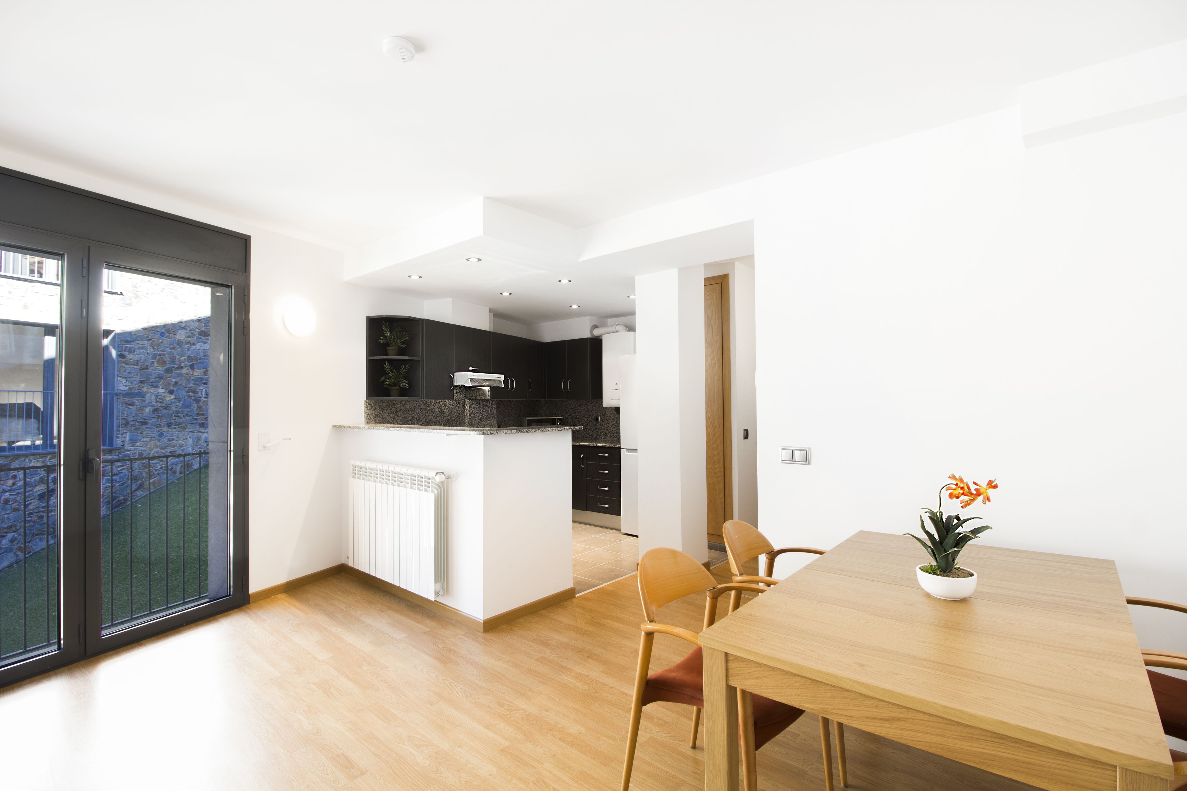 A modern kitchen with a central island, a dining area with a wooden table and chairs, and a large sliding glass door leading to a balcony.