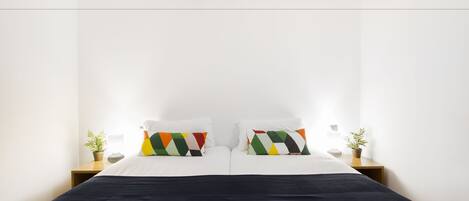 A modern hotel room with a large bed, white walls, and two bedside tables with potted plants.