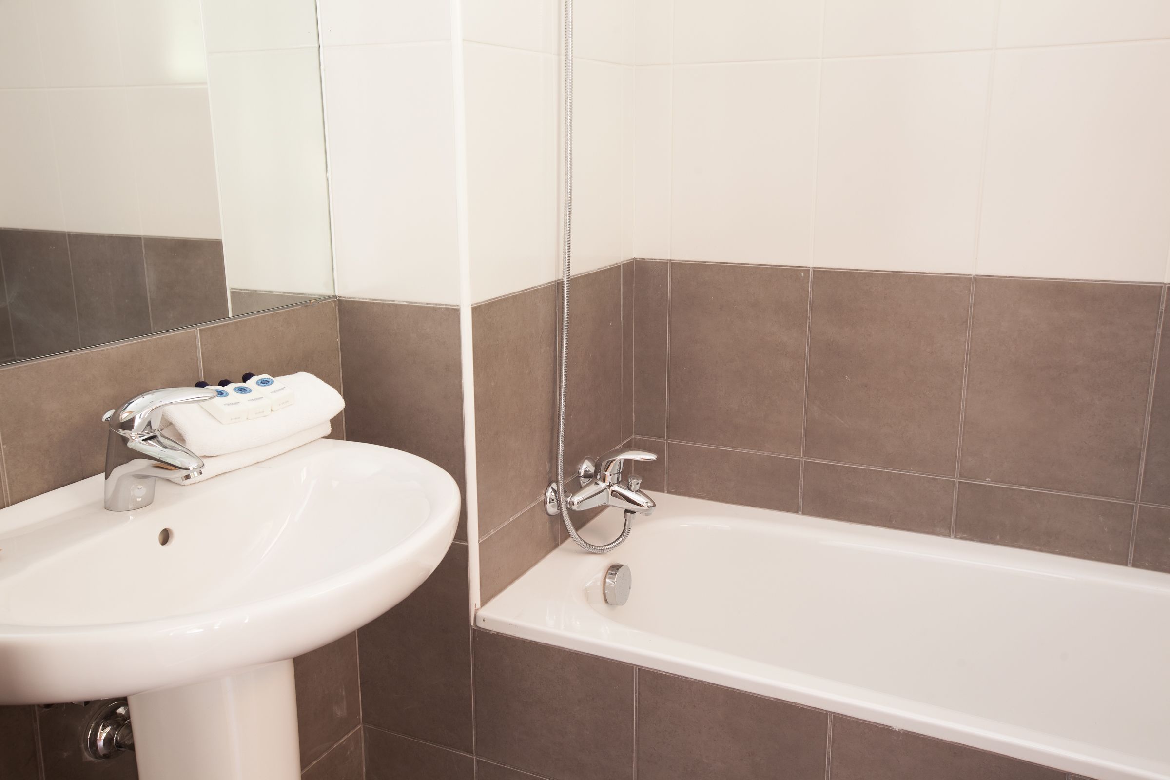 A bathroom with a white sink, a bathtub, and brown-tiled walls.
