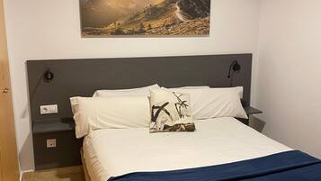 Een slaapkamer met een bed, nachtkastje, een wandlamp en een schilderij van een berglandschap.