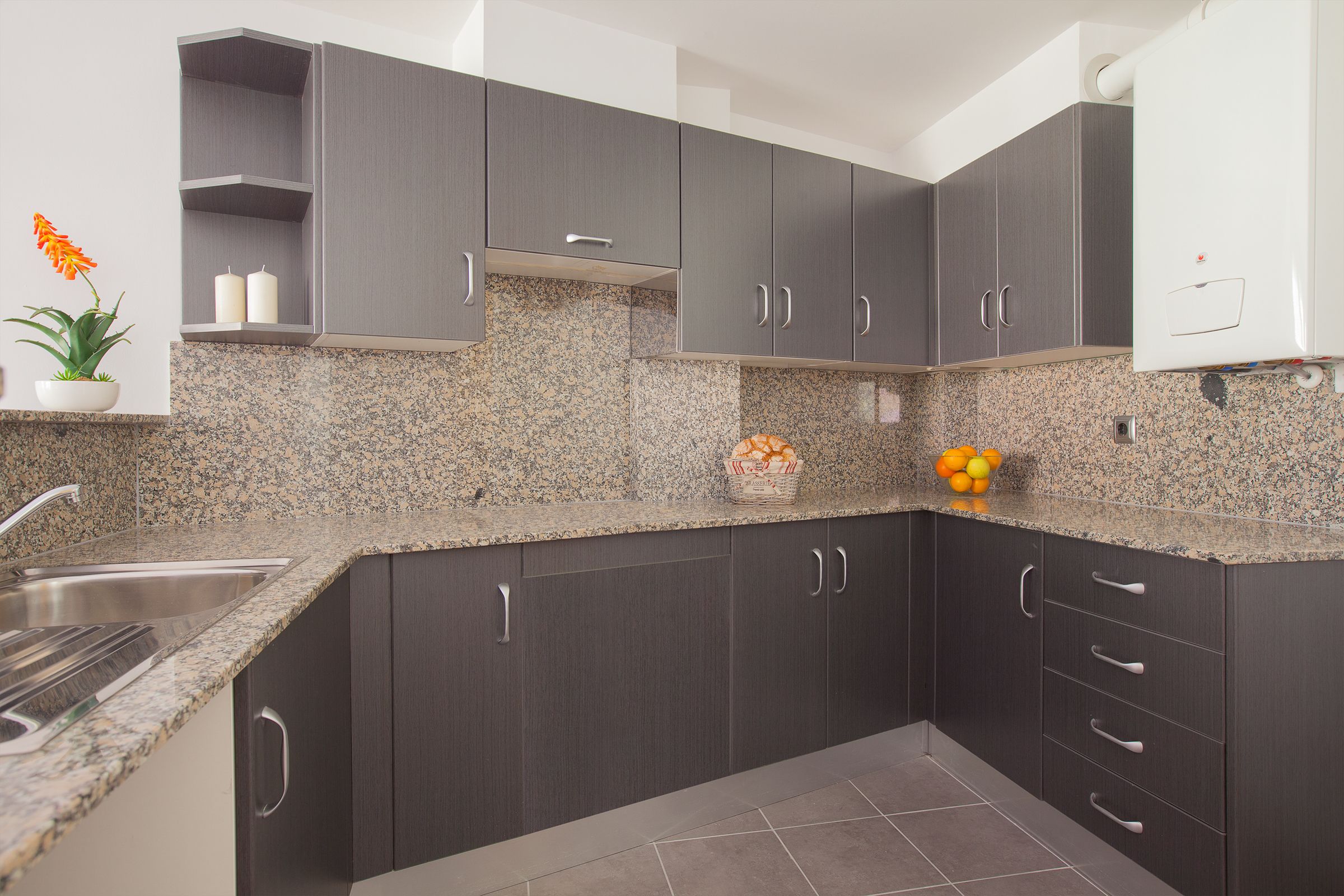 A modern kitchen with dark cabinets, granite countertops, and a stainless steel sink.
