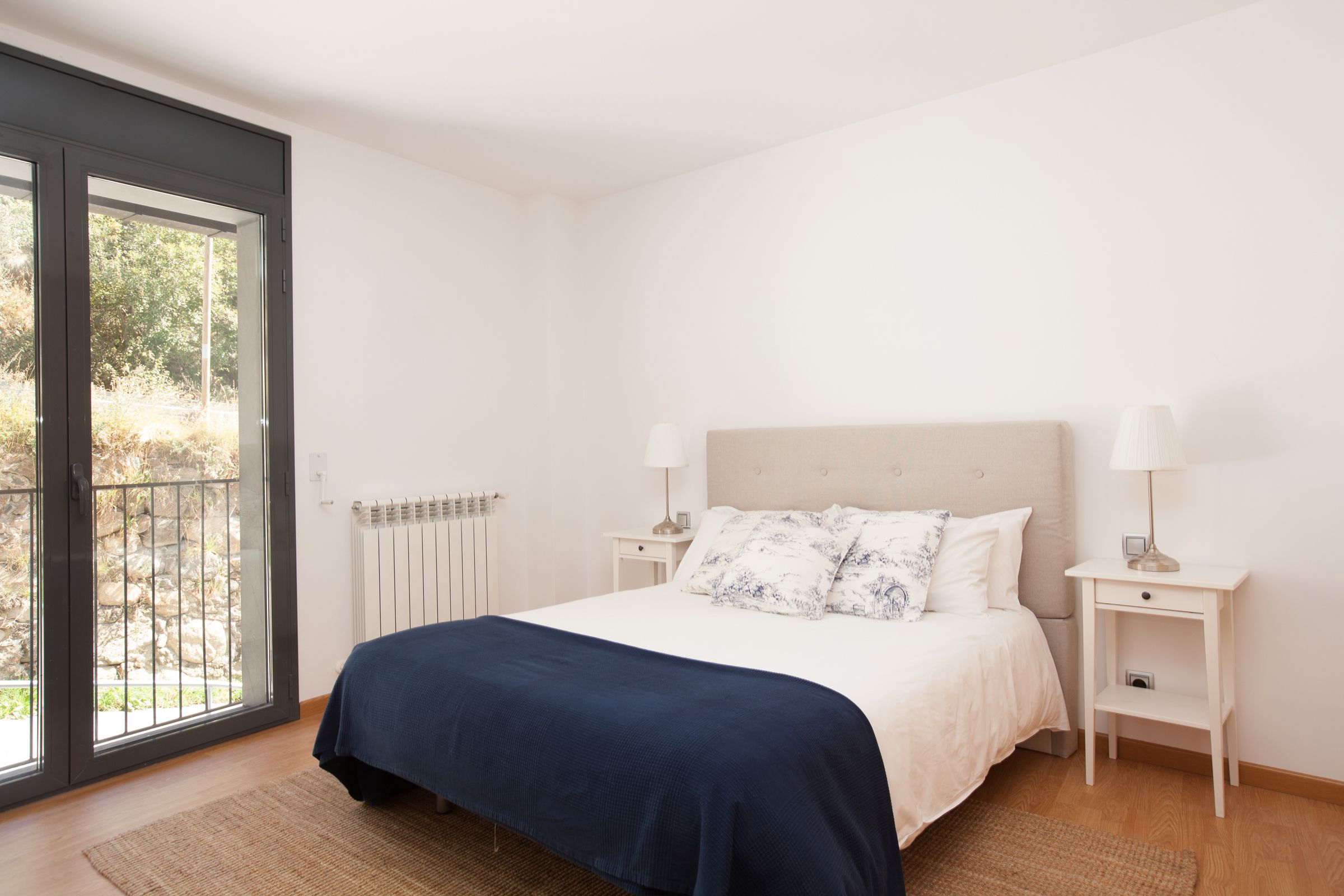 Een slaapkamer met een bed, twee nachtkastjes, een radiator en uitzicht door een glazen deur.