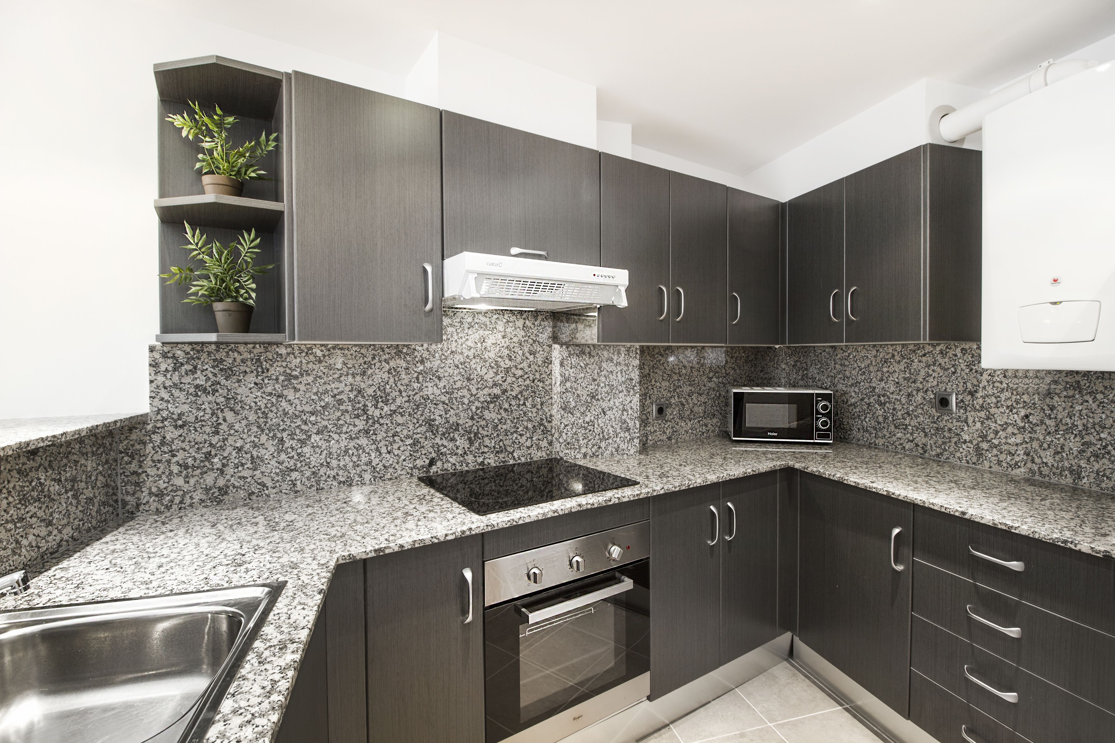 Una cocina moderna con armarios oscuros, encimeras de granito, un microondas integrado y un lavabo de acero inoxidable.