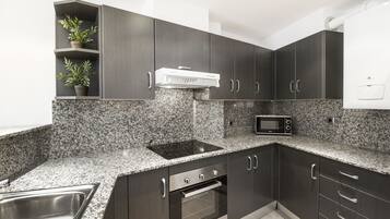 Una cocina moderna con armarios oscuros, encimeras de granito, un microondas integrado y un lavabo de acero inoxidable.