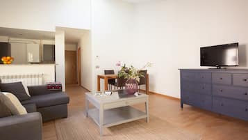 A modern living room with a grey sofa, a coffee table, a TV, and a dining area with chairs and a table.