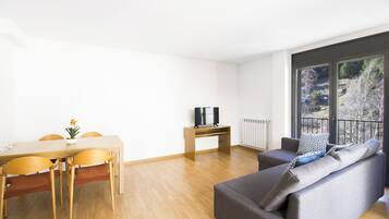 Un salon moderne avec une table à manger en bois, un canapé gris et un téléviseur posé sur un meuble en bois.