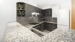 A modern kitchen with granite countertops, dark cabinetry, a built-in microwave, and a stainless steel sink. - Font del Ferro Apartaments (Ransol)