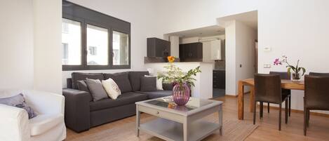 A modern living room with a grey sofa, a glass coffee table, and a dining area with a wooden table and chairs.
