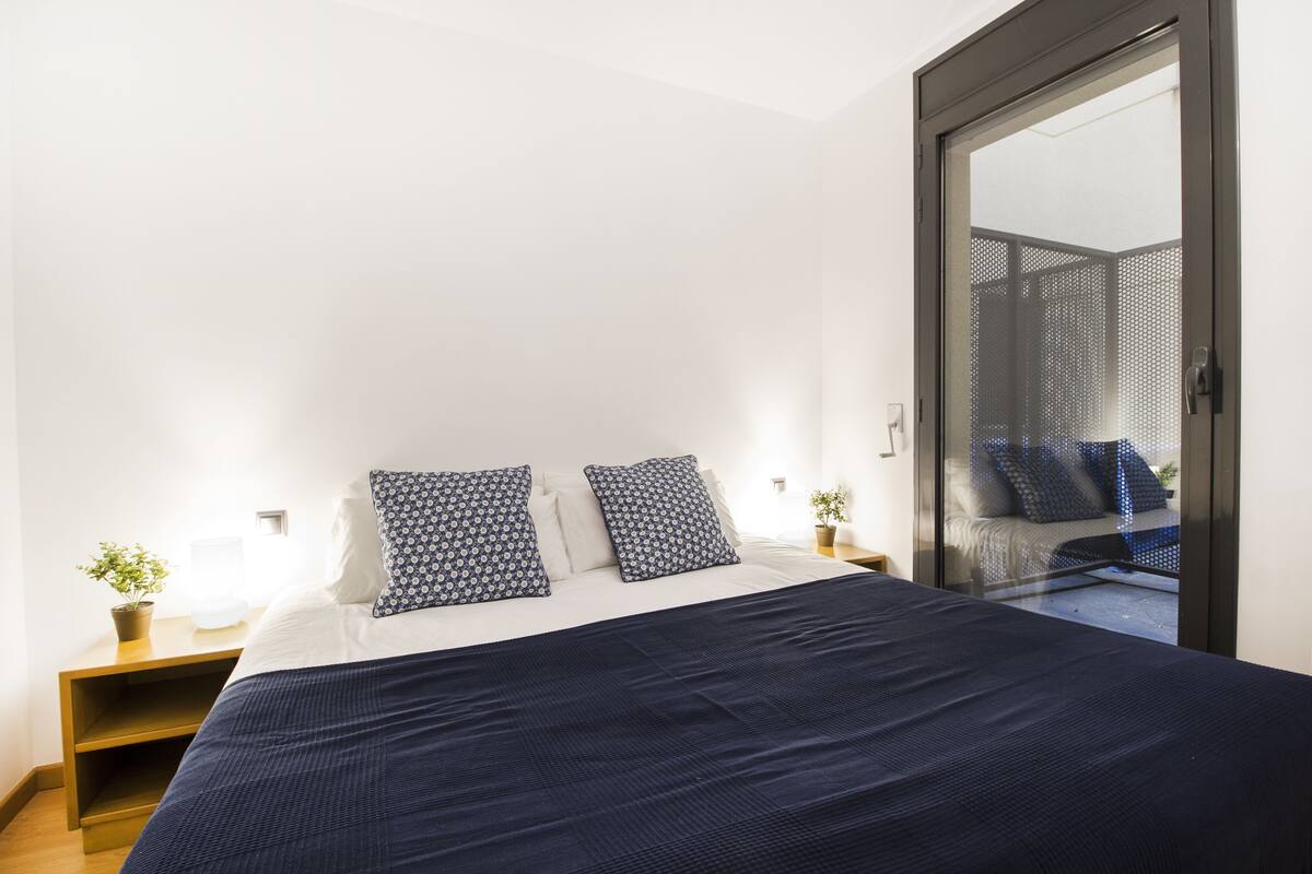 A bedroom with a large bed, two bedside tables, and a sliding glass door leading to a balcony.