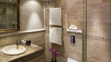 A modern bathroom with a marble sink, a large mirror, a glass shower enclosure, and a potted orchid.