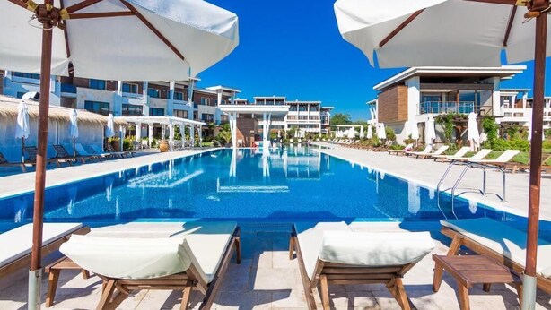 A swimming pool with lounge chairs and umbrellas, surrounded by modern buildings. - Apolonia Resort (Sozopol)