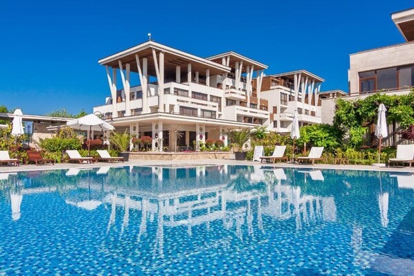 A modern hotel with a large pool, multiple balconies, and outdoor seating areas. - Apolonia Resort (Sozopol)