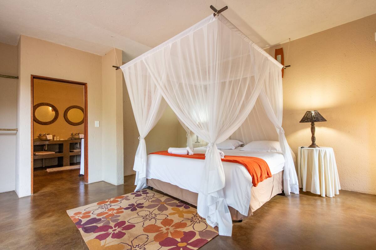 A bedroom with a four-poster bed, a bedside table with a lamp, and a floral rug.