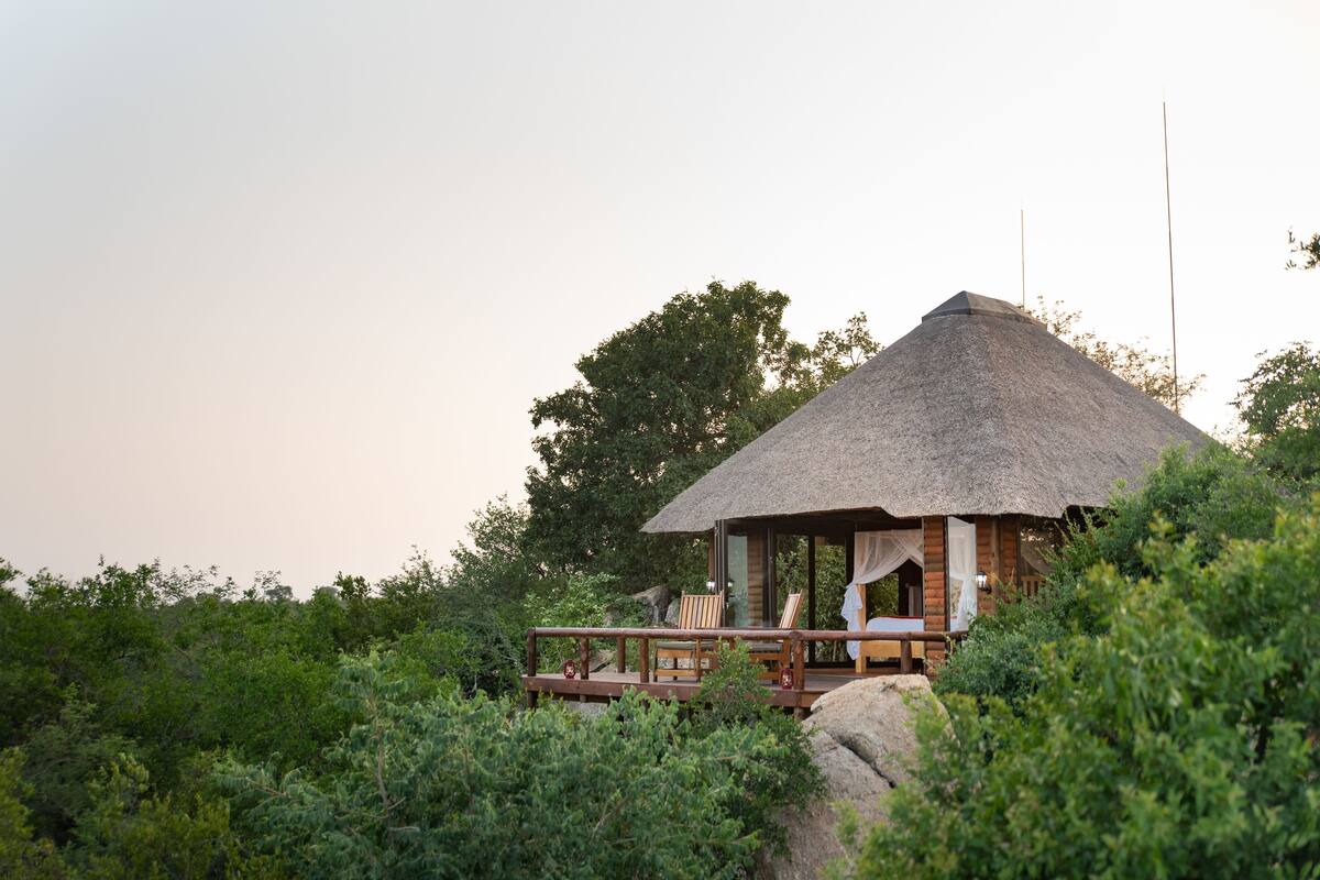 A thatched-roof hut with a wooden deck, surrounded by lush greenery.