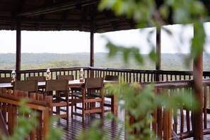 An outdoor wooden deck with a table and chairs, overlooking a hilly landscape. - Elephant Game Lodge (Hoedspruit)